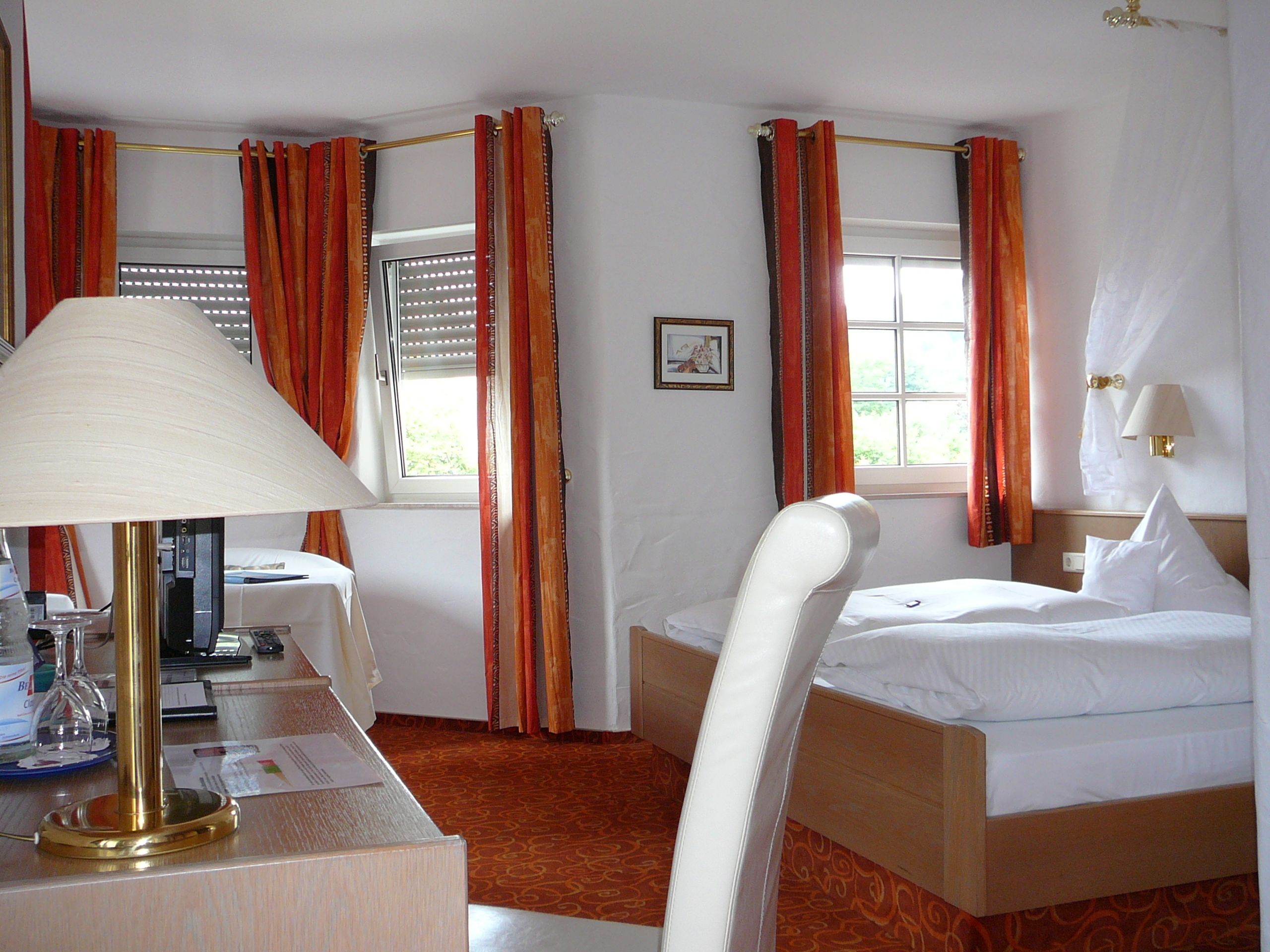 A hotel room with a bed, a desk with a lamp, a chair, and a window with curtains.