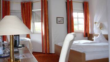 A hotel room with a bed, a desk with a lamp, a chair, and a window with curtains.