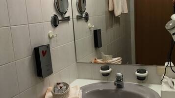 Une salle de bain avec un grand lavabo, deux miroirs, un porte-serviettes, un distributeur de savon et un sèche-cheveux.