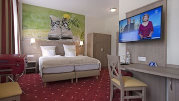 A hotel room with a bed, a desk, a television, and a mural on the wall.