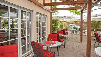 An outdoor patio with red chairs and tables, umbrellas, and a brick floor.