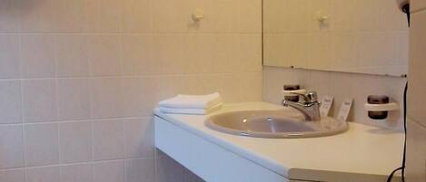 Baño con lavamanos blanco, espejo y suelo de baldosas.