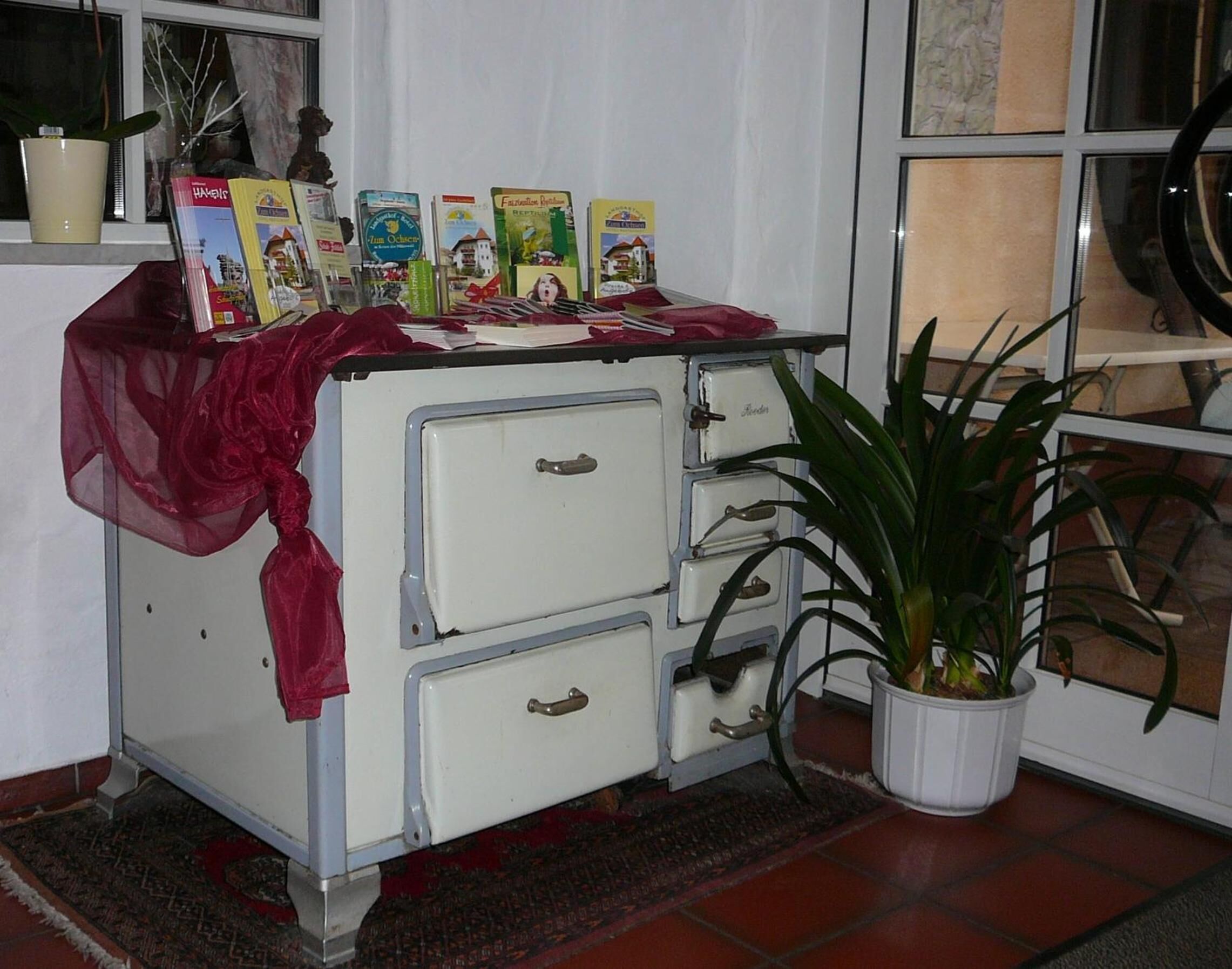 A vintage white chest of drawers with a red cloth, a potted plant, and travel brochures on top.