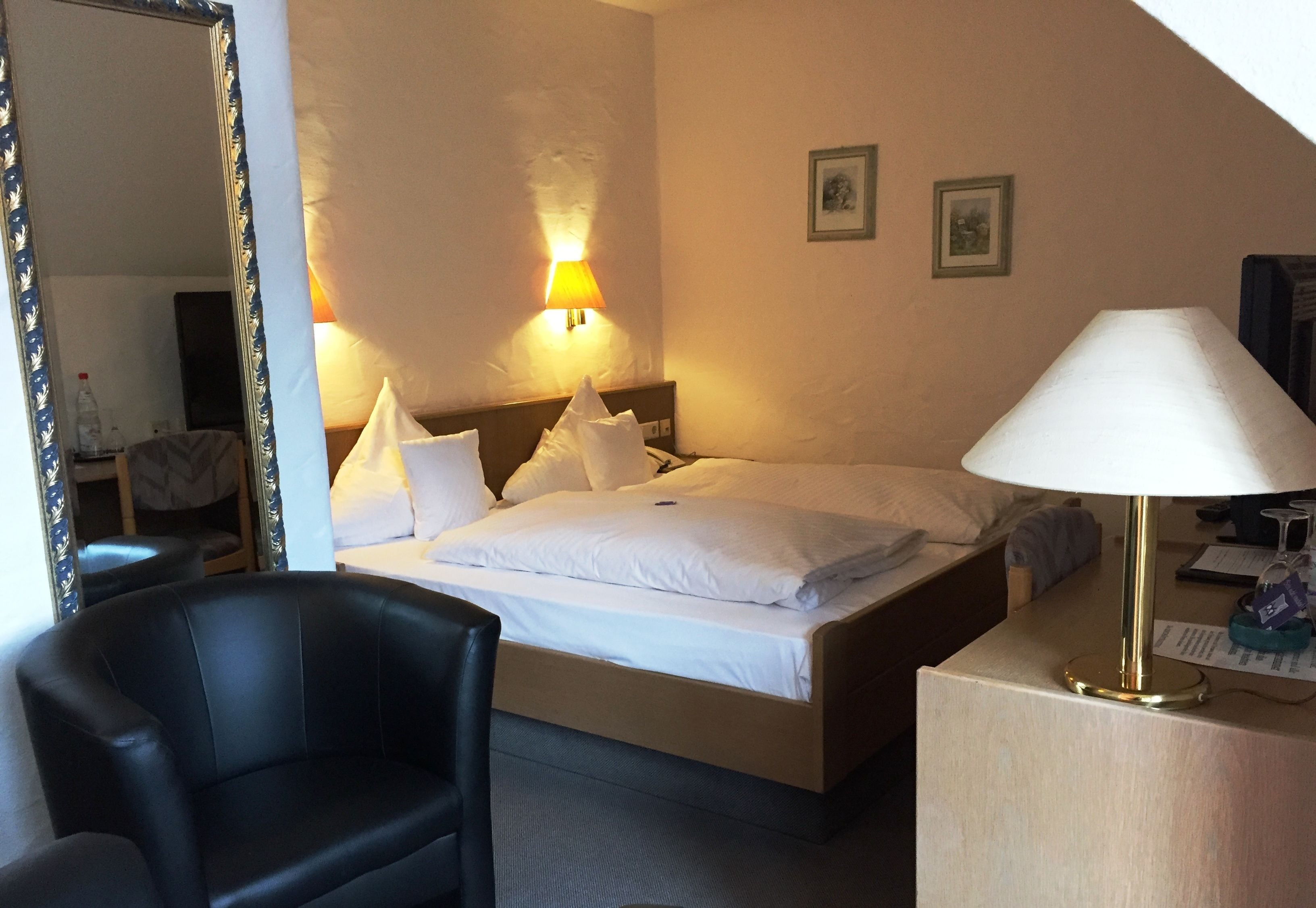 Quarto de hotel com cama, escrivaninha com luminária, cadeira e espelho.