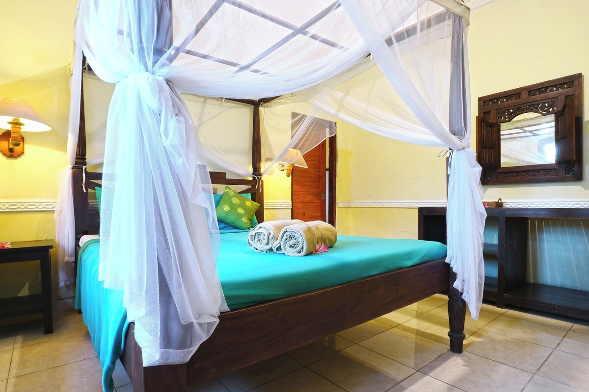 A four-poster bed with a green bedspread, a wooden headboard, and a mirror above it.
