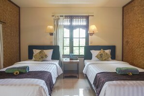 A hotel room with two beds, a window with curtains, and two wall-mounted lamps. - Ubud Kerta City Hotel (Ubud)