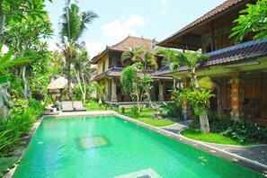 Ein traditionelles Haus mit Swimmingpool, umgeben von üppiger Vegetation.