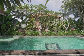 A rectangular pool with clear water, surrounded by lush greenery and a stone statue. - Ubud Kerta City Hotel (Ubud)