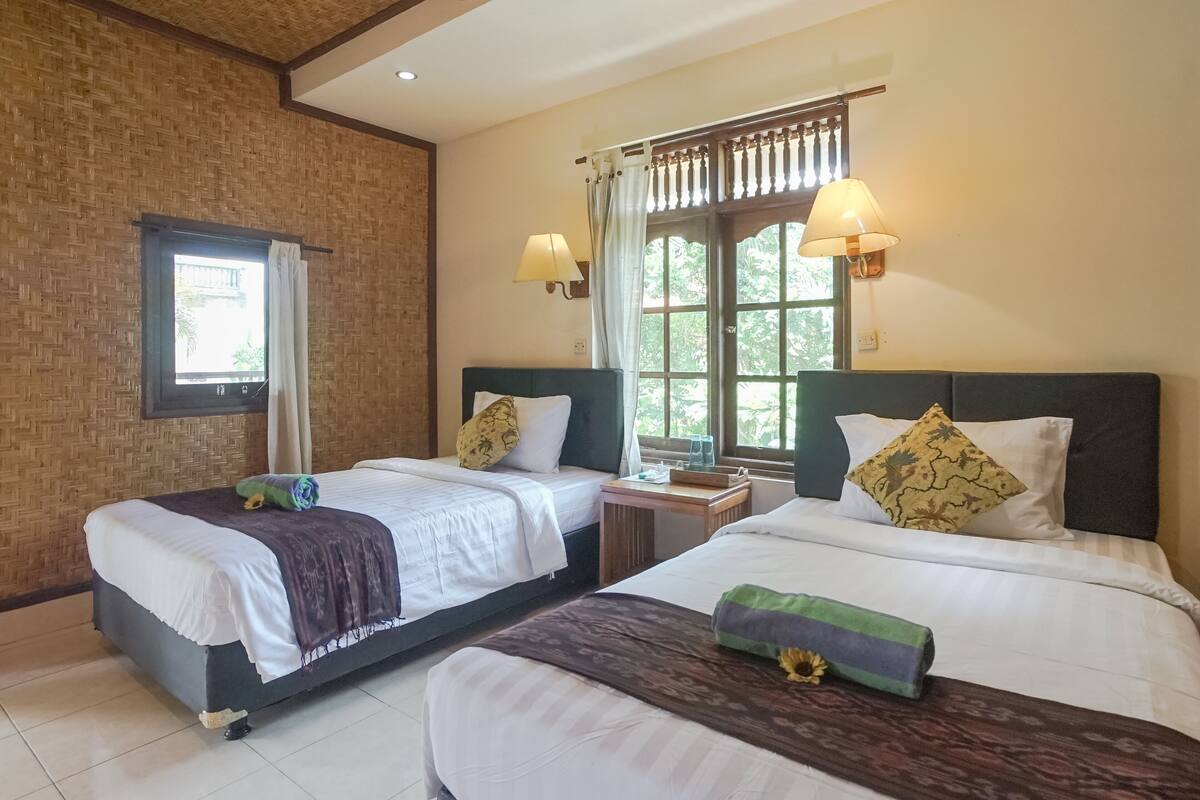 A hotel room with two beds, a window with curtains, a nightstand, and wall-mounted lamps.