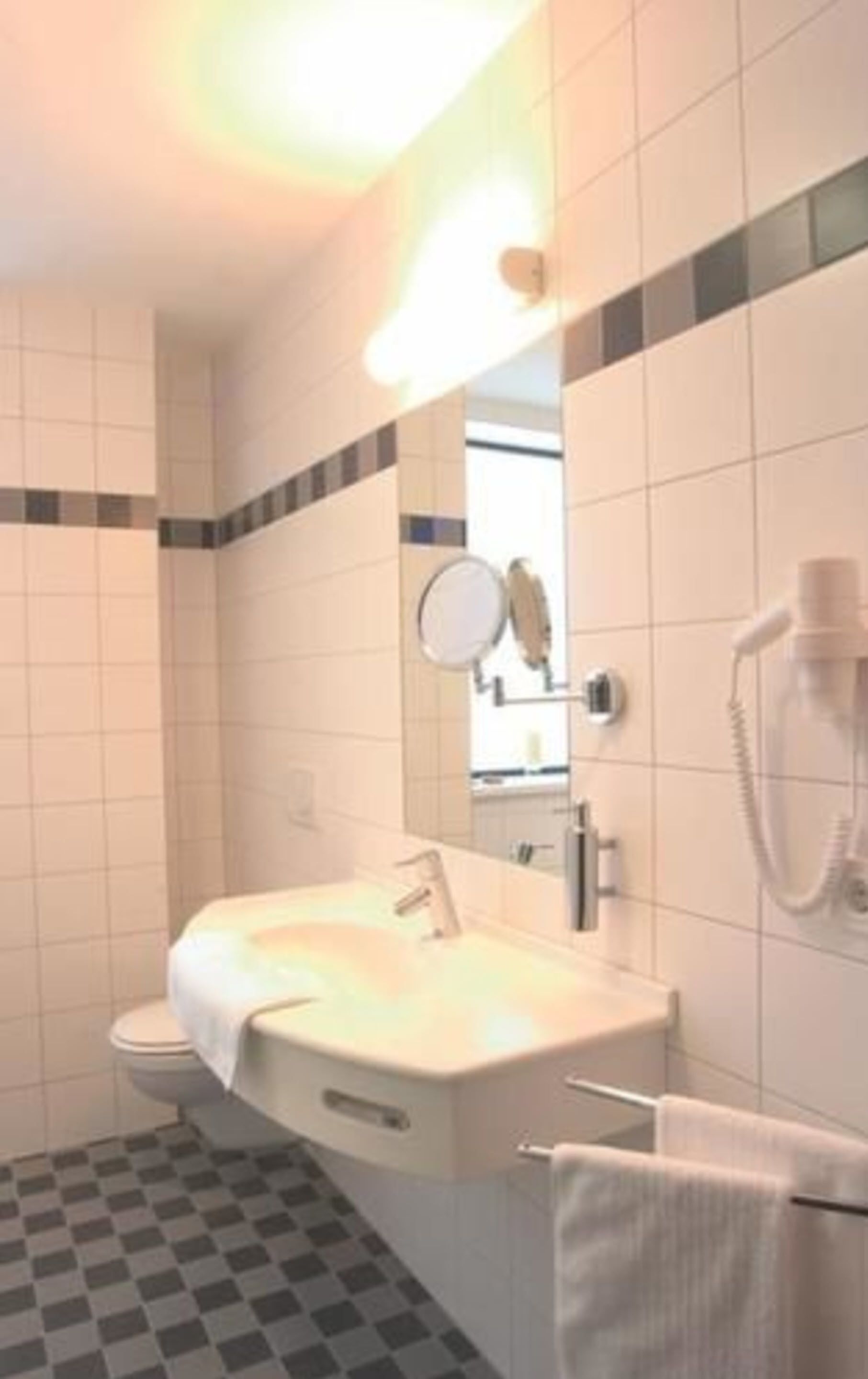 Ein Badezimmer mit weißem Waschbecken, einem Spiegel, einem Handtuchhalter und einer Dusche.