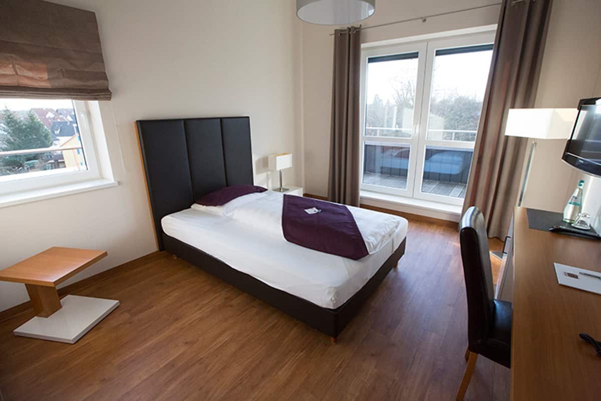 A hotel room with a bed, a desk, a chair, a window, and a view of the outside.
