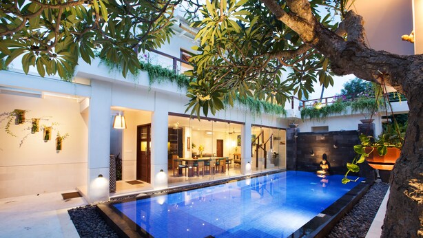 A modern indoor swimming pool with a glass enclosure, surrounded by a patio area with seating and a dining space. - Sunset Paradise Villa Jimbaran 3003 (Kedonganan)