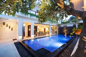 A modern indoor swimming pool with a glass enclosure, surrounded by a patio area with seating and a dining space.