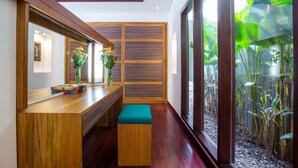 A modern interior with a wooden bench, a small table with a vase of flowers, and a large window with a view of plants. - Sunset Paradise Villa Jimbaran 3003 (Kedonganan)