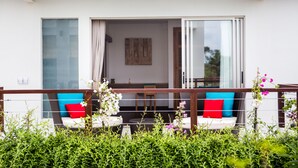 A balcony with a wooden railing, two white sofas with red and blue cushions, and a glass door leading to an interior space. - Sunset Paradise Villa Jimbaran 3003 (Kedonganan)