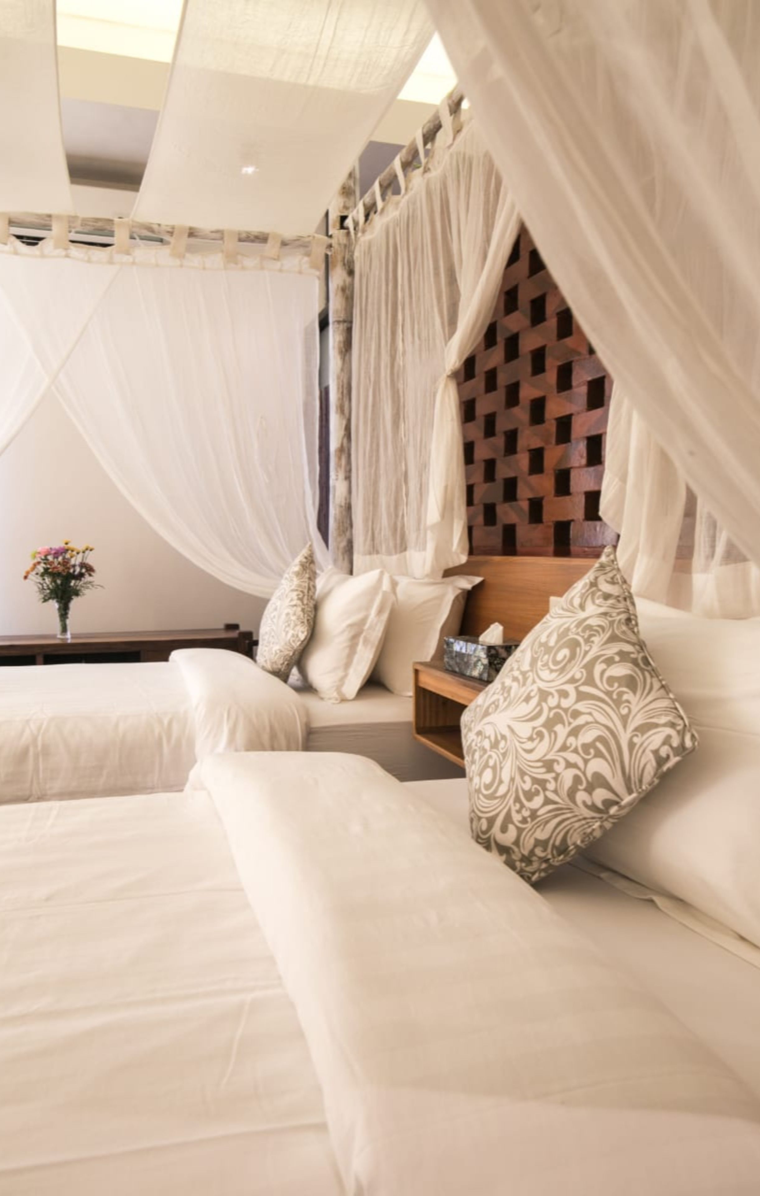 Un dormitorio con cama a dosel, cabecera de madera y mesita de noche con un jarrón de flores.