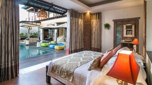A bedroom with a large bed, a ceiling fan, a red lamp, and a view of an outdoor pool area. - Sunset Paradise Villa Temple Hill (Jimbaran)