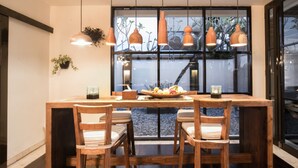 A dining area with a wooden table and chairs, pendant lights, and a window with a view of greenery. - Sunset Paradise Villa Temple Hill (Jimbaran)