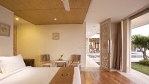 A modern hotel room with a wooden ceiling, a large bed, two chairs, a small table, and a view of the outside. - Sunset Paradise Villa Uluwatu (Pecatu)