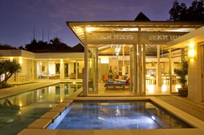 A modern resort with a glass-enclosed lounge area, a swimming pool, and a dining area. - Sunset Paradise Villa Uluwatu (Pecatu)