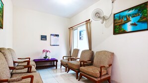 A living room with four armchairs, a glass coffee table, a purple bench, and a wall-mounted fan. - Casa Sidoluhur 17 (Surabaya)