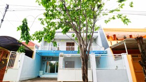 A residential building with a blue and white facade, a gated entrance, and a tree in the foreground. - Casa Sidoluhur 17 (Surabaya)