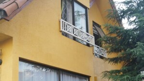 Una casa de dos plantas con fachada amarilla, ventanas amplias y un balcón pequeño.