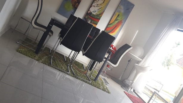 Un interior moderno con piso de baldosas, una zona de comedor con sillas negras y obras de arte coloridas en las paredes.