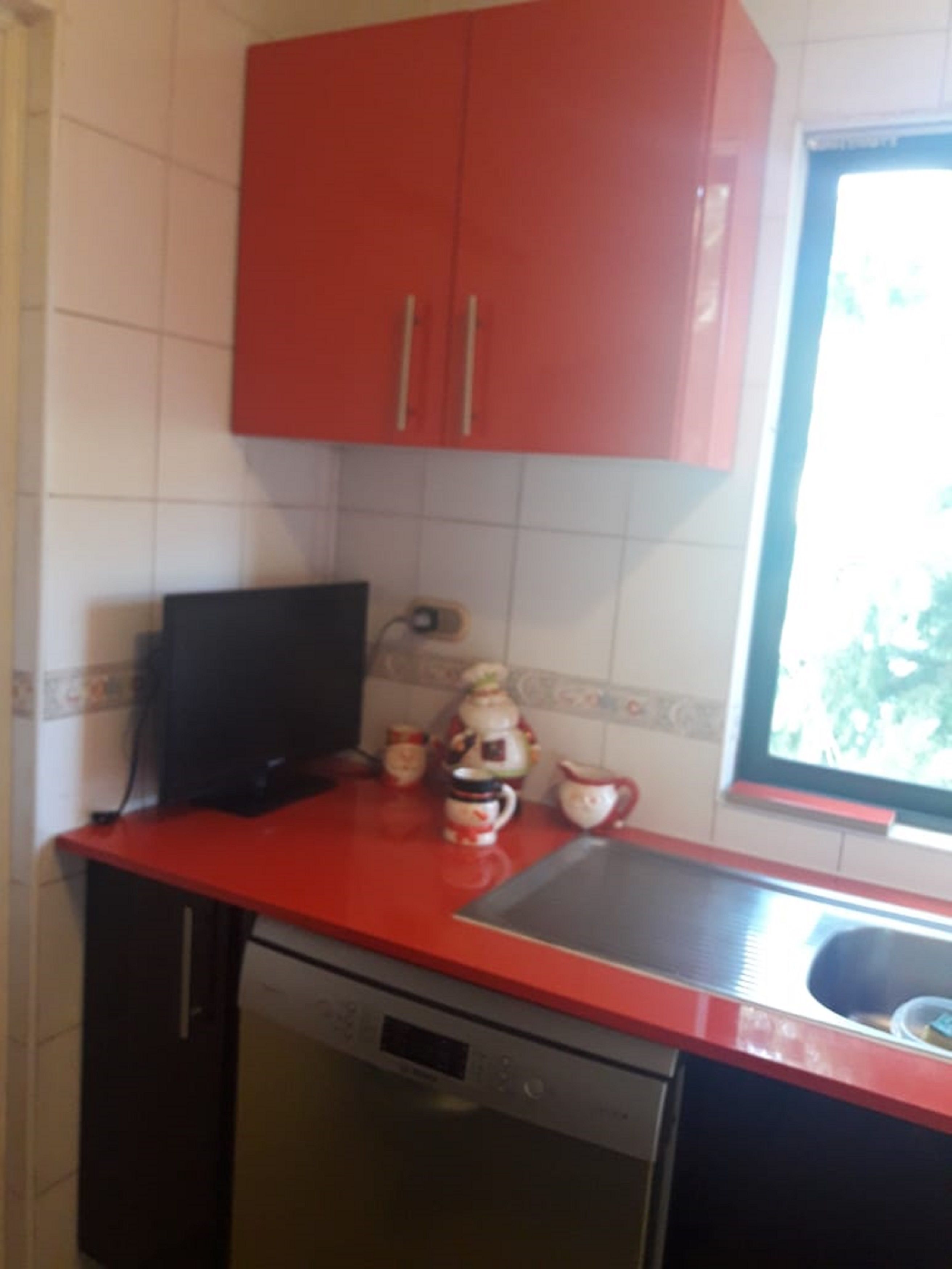 Eine Küche mit roten Schränken, einer schwarzen Arbeitsplatte, einem Geschirrspüler und einem Fenster mit Blick.
