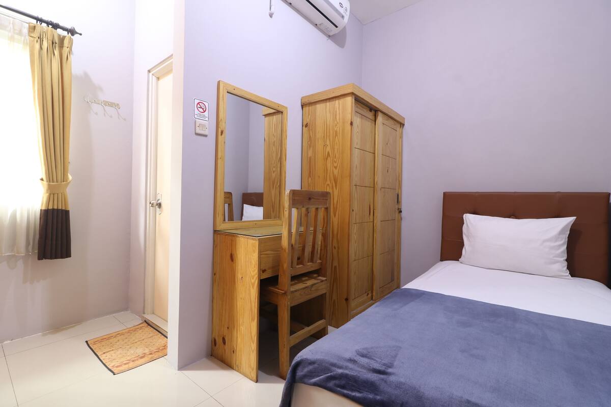 Un dormitorio con una cama, un armario de madera, un espejo, un escritorio y una zona de ducha.