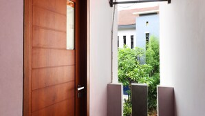 A wooden door with a small window, a metal gate, and a view of a building and greenery in the background. - Bedur Homestay Syariah (Bekasi)