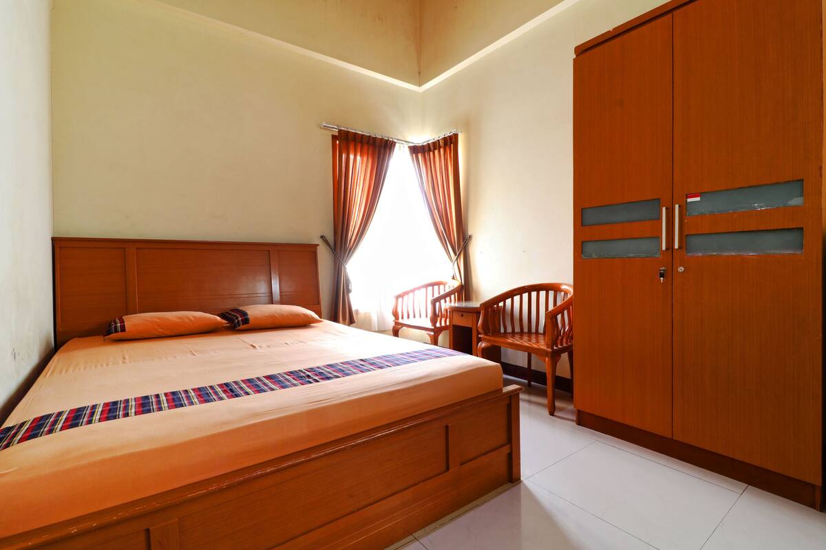 Un dormitorio con cama de madera, un armario, una silla y una ventana con cortinas.