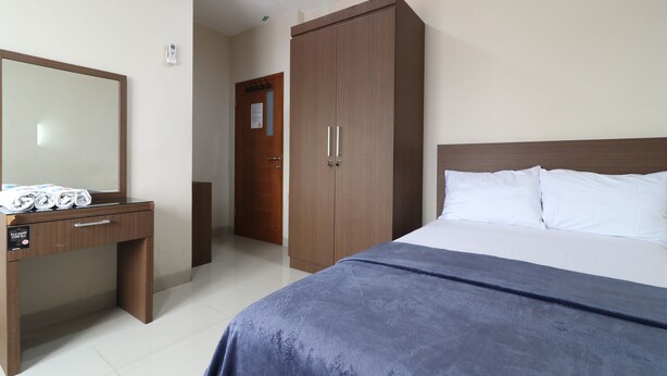 A bedroom with a bed, a wooden wardrobe, a desk with a mirror, and a door leading to another room. - Bedur Homestay Syariah (Bekasi)