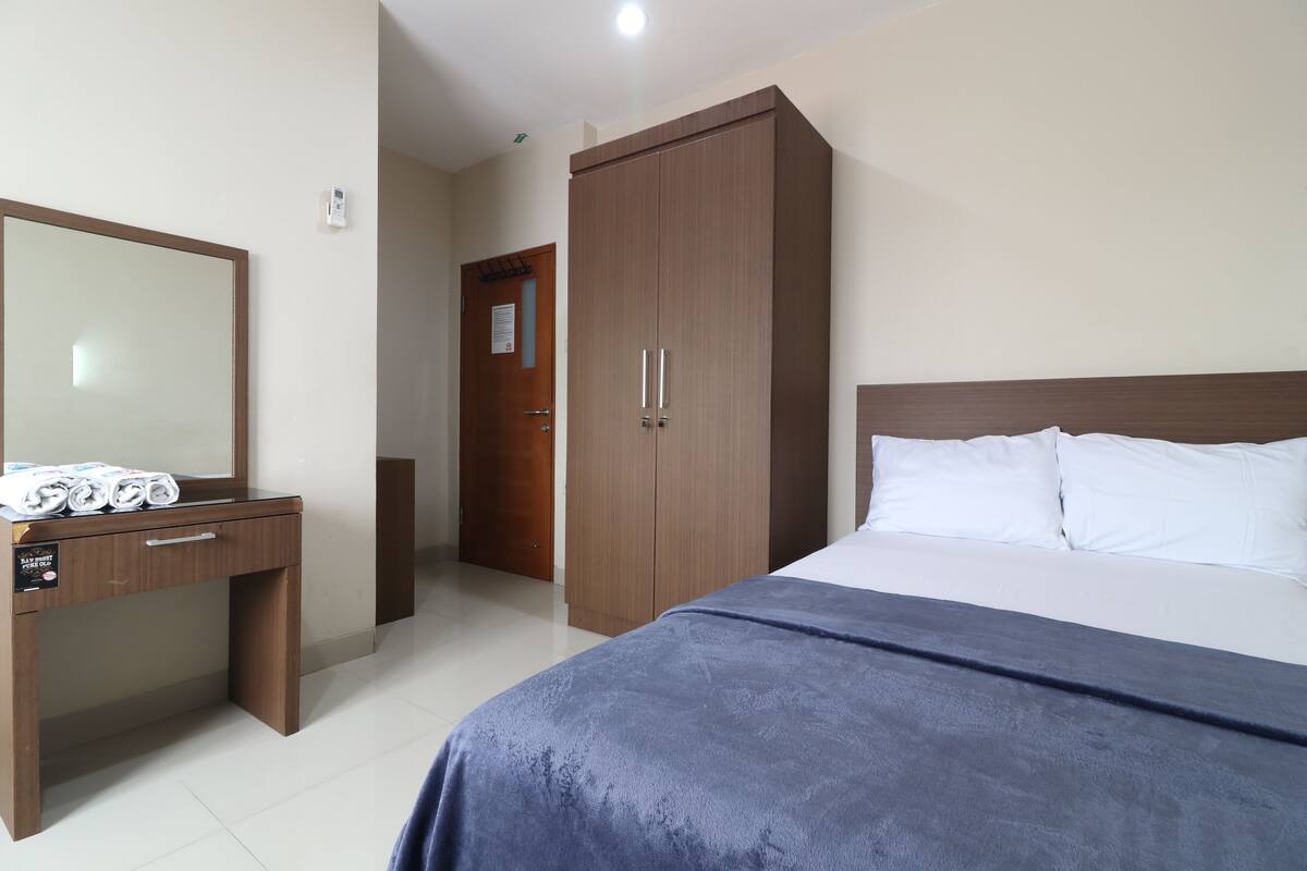 Un dormitorio con cama, un armario de madera, un escritorio con espejo y una puerta que da a otra habitación.