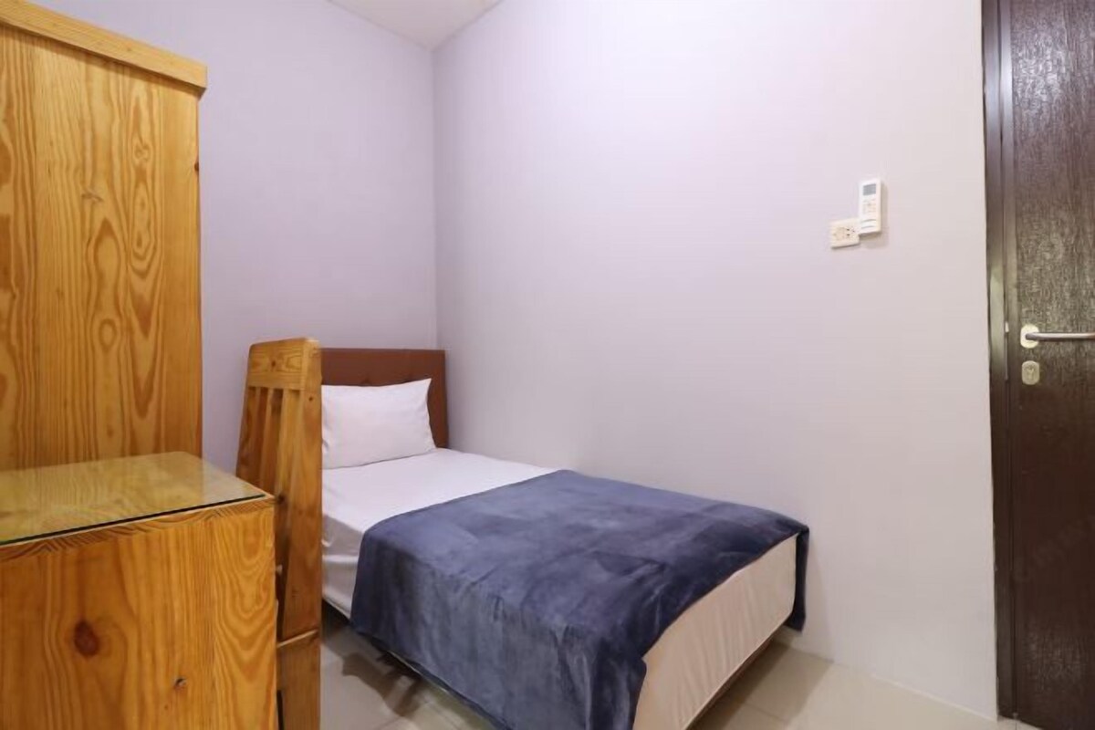 A small, neatly arranged bedroom with a single bed, a wooden wardrobe, and a door.