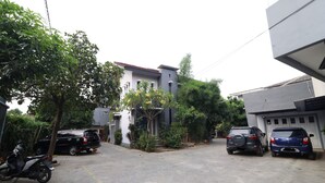 A residential street with parked cars and a motorcycle, surrounded by trees and houses. - Bedur Homestay Syariah (Bekasi)