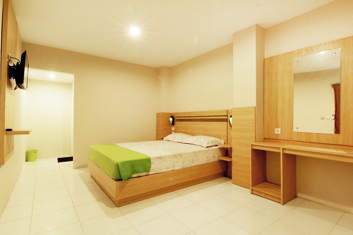A bedroom with a wooden bed, a bedside table, a mirror, and a green trash bin.