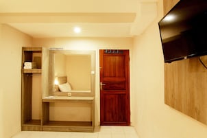 Habitación de hotel con un armario de madera, un espejo, un televisor montado en la pared y un pequeño estante con toallas.