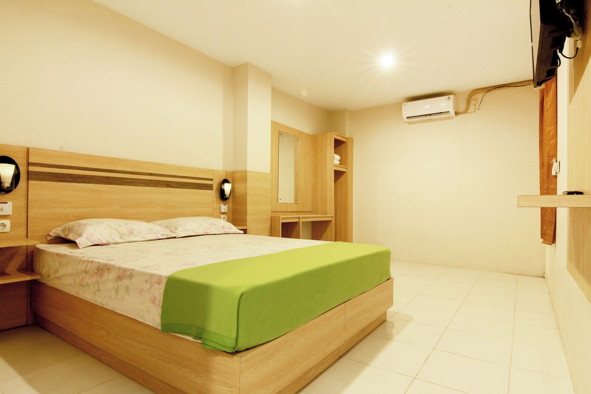 A bedroom with a wooden bed, a nightstand, a green bedspread, a wall-mounted air conditioner, and a wooden wardrobe.