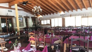 A restaurant with wooden beams and tables set with pink napkins and wine glasses. - El Palacil (Velez-Blanco)