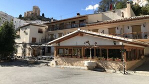 A building with a balcony, a stone bench, and a sign. - El Palacil (Velez-Blanco)