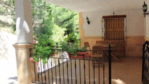 A covered outdoor seating area with a wrought iron fence, potted plants, and a wooden table and chairs. - El Palacil (Velez-Blanco)