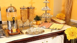 Un buffet de petit-déjeuner comprenant un distributeur de jus, des récipients de céréales, un présentoir à étages pour les desserts et une composition florale.