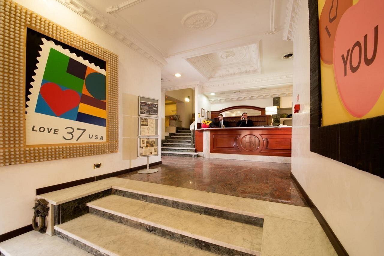 Un vestíbulo de hotel con mostrador de recepción, una escalera y una llamativa obra de arte en la pared.