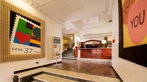 Un hall d’hôtel comprenant un comptoir d’accueil, un escalier et une œuvre d’art murale aux couleurs vives.