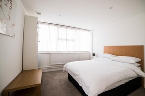 A bedroom with a bed, a wooden bench, a radiator, and a window with blinds.
