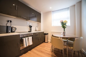 A modern kitchen with dark cabinets, a stainless steel range hood, a built-in oven, and a small dining area with a round table and chairs.
