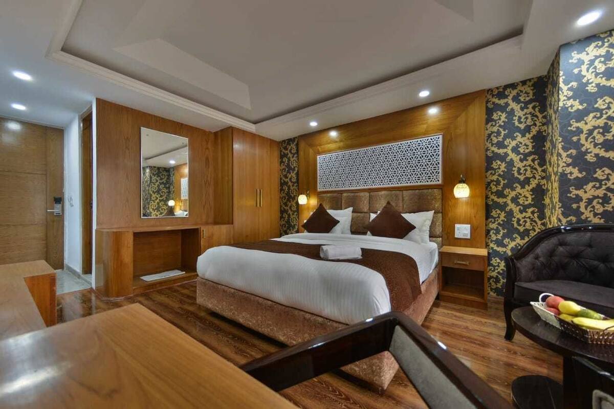 Quarto de hotel com cama grande, painéis de madeira, cabeceira decorativa e sofá de couro preto.