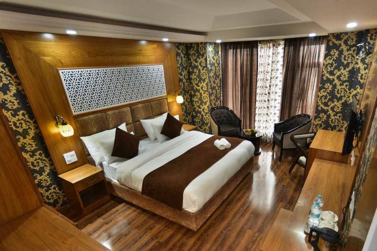 Quarto espaçoso com uma cama grande, escrivaninha e cadeira, piso de madeira e papel de parede estampado.