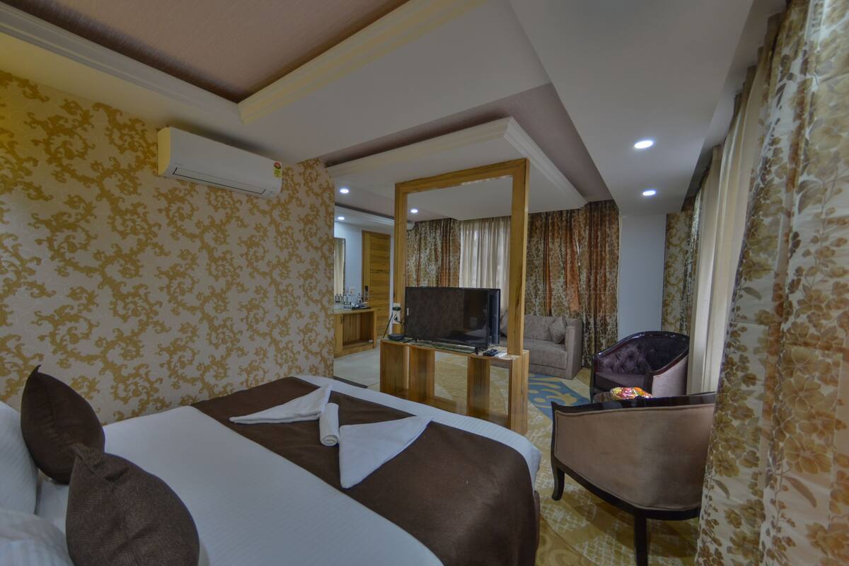 Quarto de hotel com cama, televisão, secretária com cadeira e espelho.